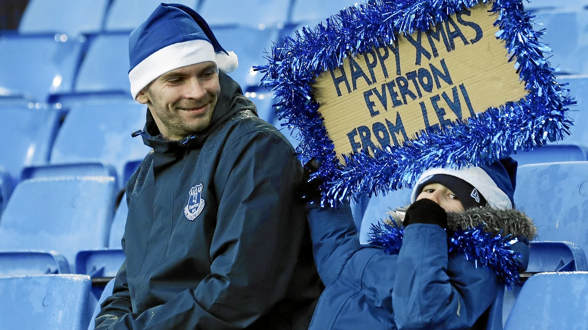 Un niño muestra una pancarta de feliz Navidad en el campo del Everton