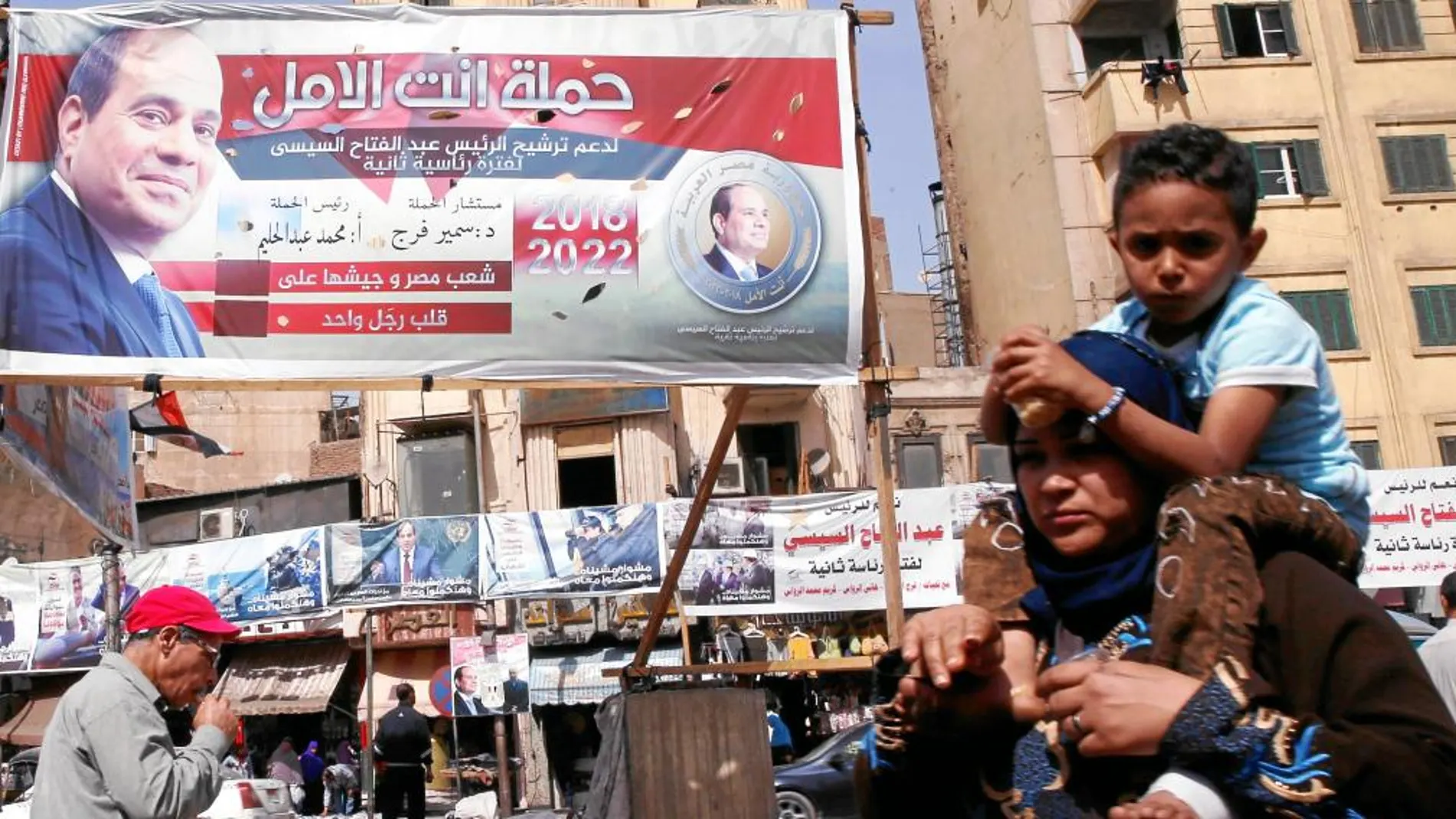 Varias personas caminan por una calle de El Cairo junto a un cartel con la imagen del presidente egipcio Al Sisi