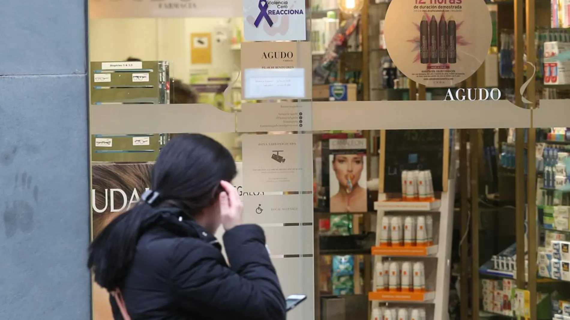 Una mujer pasa frente a una farmacia de Valladolid con el cartel que anuncia su incorporación al programa contra esta lacra social