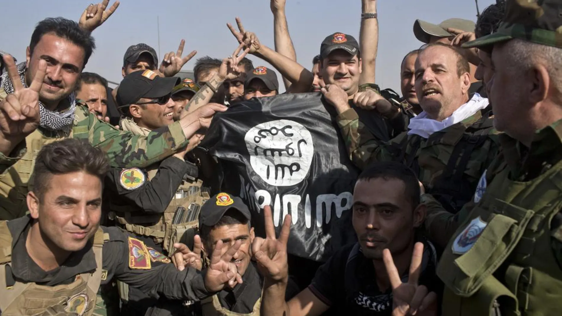 Soldaos iraquíes y kurdos con una bandera arrabatada al Estado Islámico en Bartella
