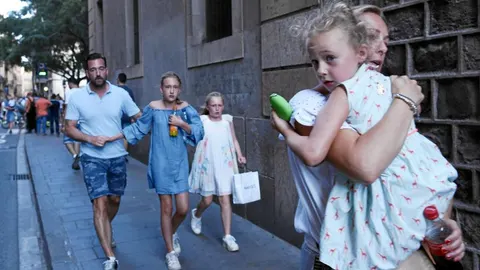 Hombres, mujeres y niños se alejan de la zona del atentado en Las Ramblas de Barcelona, ayer