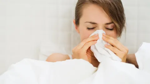 Mujer en la cama sonándose la nariz