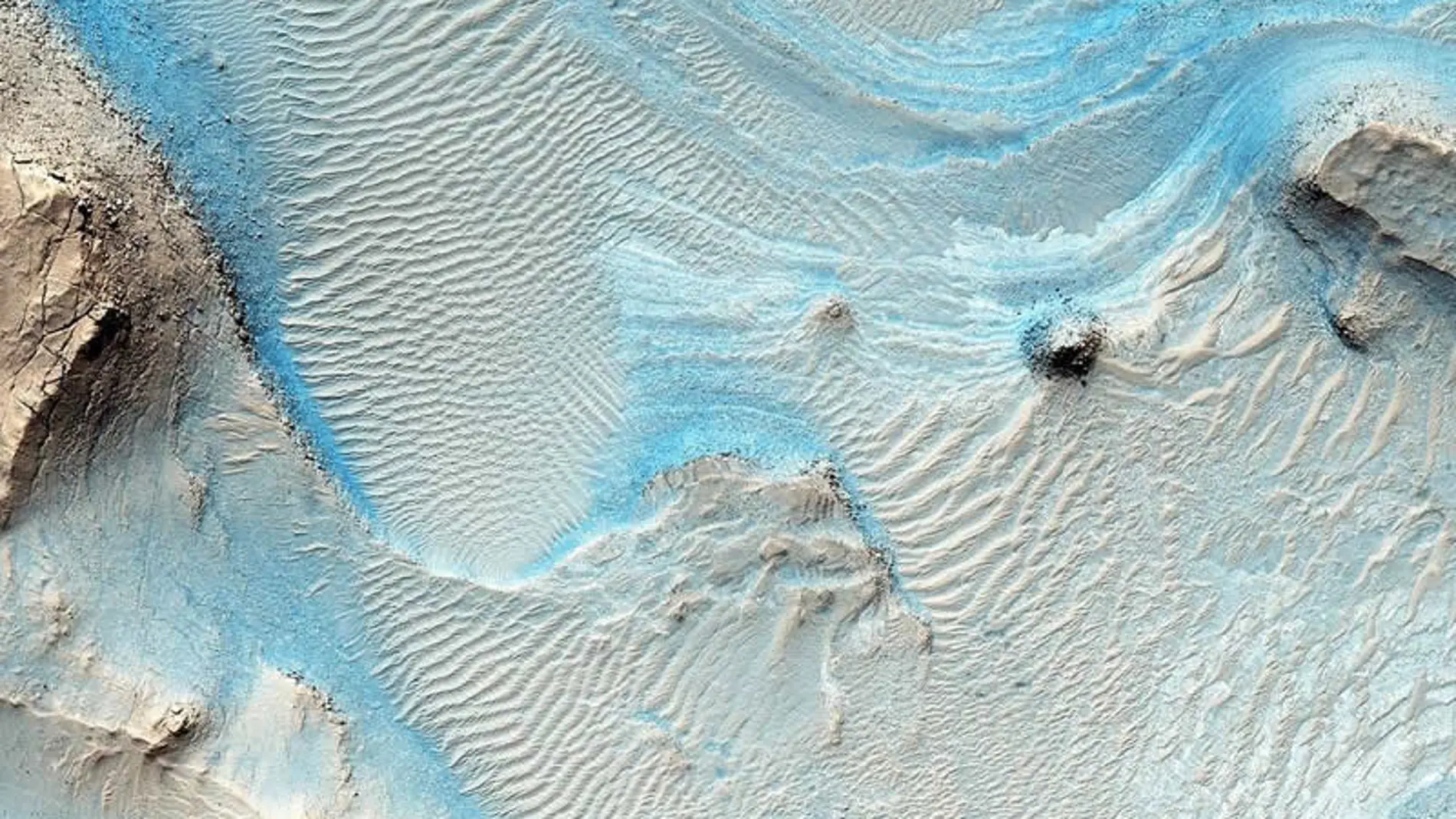 Imagen de Nili Fossae, donde puede apreciarse un lecho de roca en capas horizontales como estrías en los sedimentos de tonos claros en el suelo de un cañón cerca de Syrtis Major