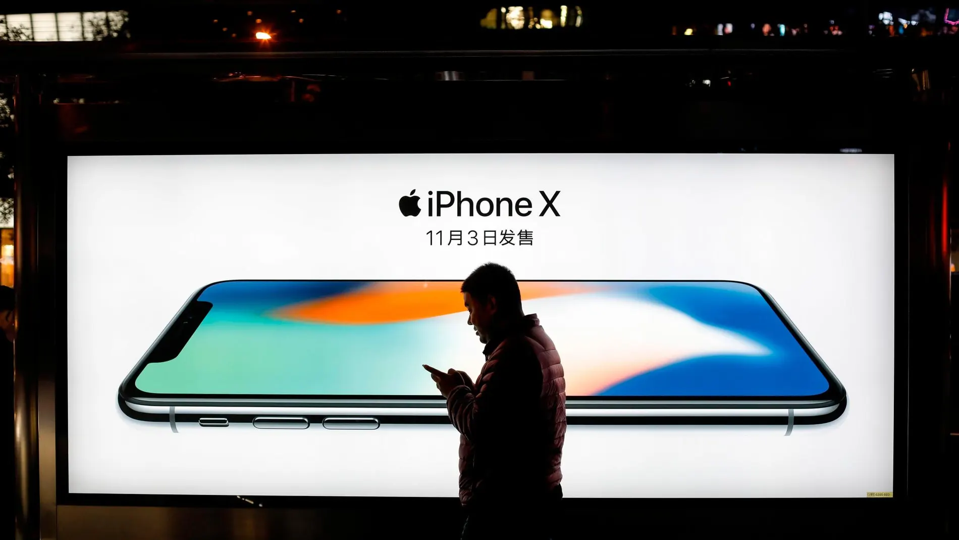 Imagen de archivo muestra a hombre mientras pasea frente a un anuncio del modelo iPhone X en Pekín (China) / EFE