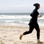Una mujer ataviada con un burkini camina por la playa.
