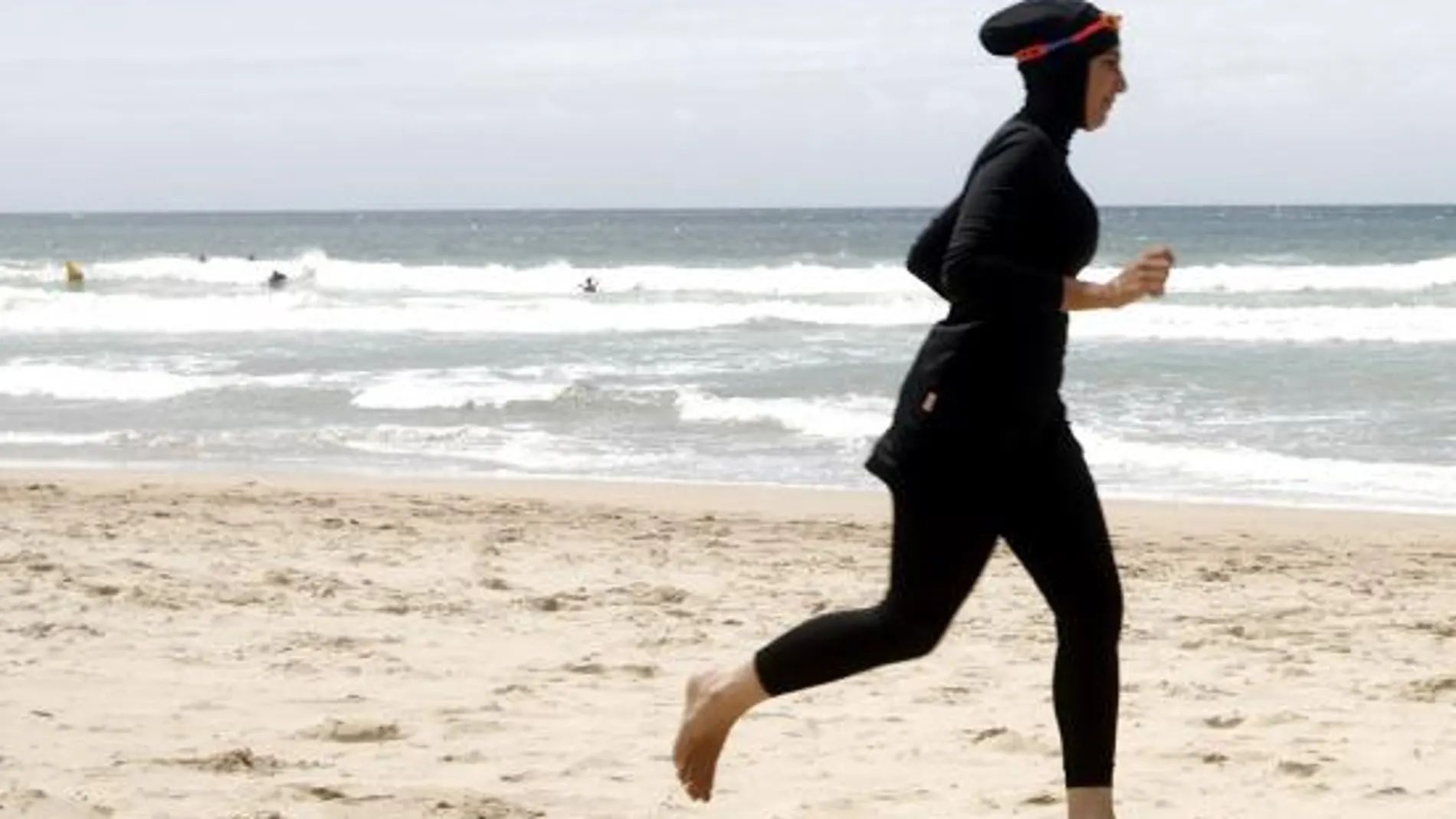 Una mujer ataviada con un burkini camina por la playa.