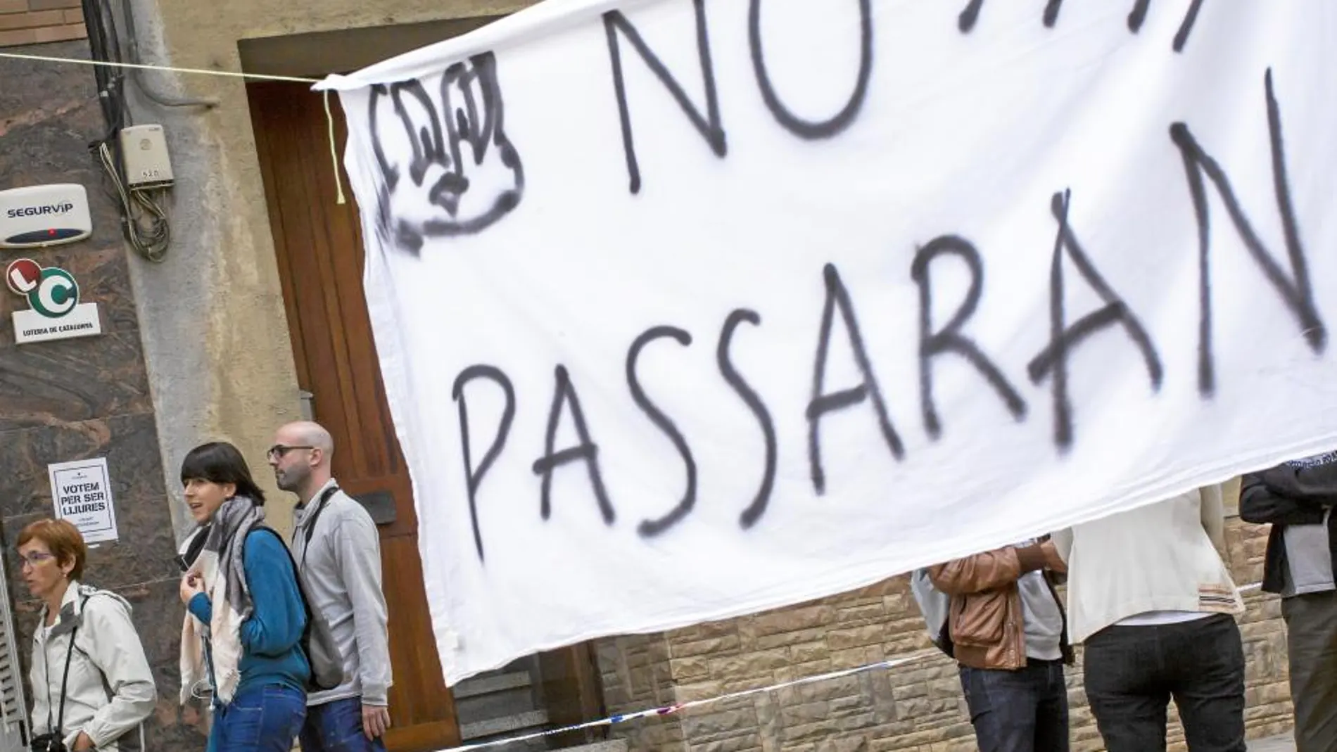 Habitantes de Arenys de Munt pasan detrás de un cartel con un «No pasarán» y un piolín dibujado
