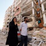 Una pareja camina entre los restos de los edificios en la zona afectada por el terremoto que asoló hace dos días la ciudad de Pole-Zahab (Irán)