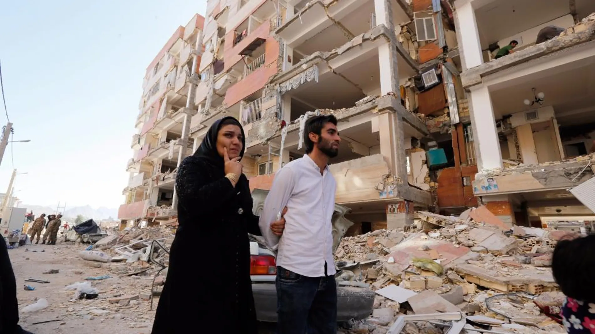 Una pareja camina entre los restos de los edificios en la zona afectada por el terremoto que asoló hace dos días la ciudad de Pole-Zahab (Irán)
