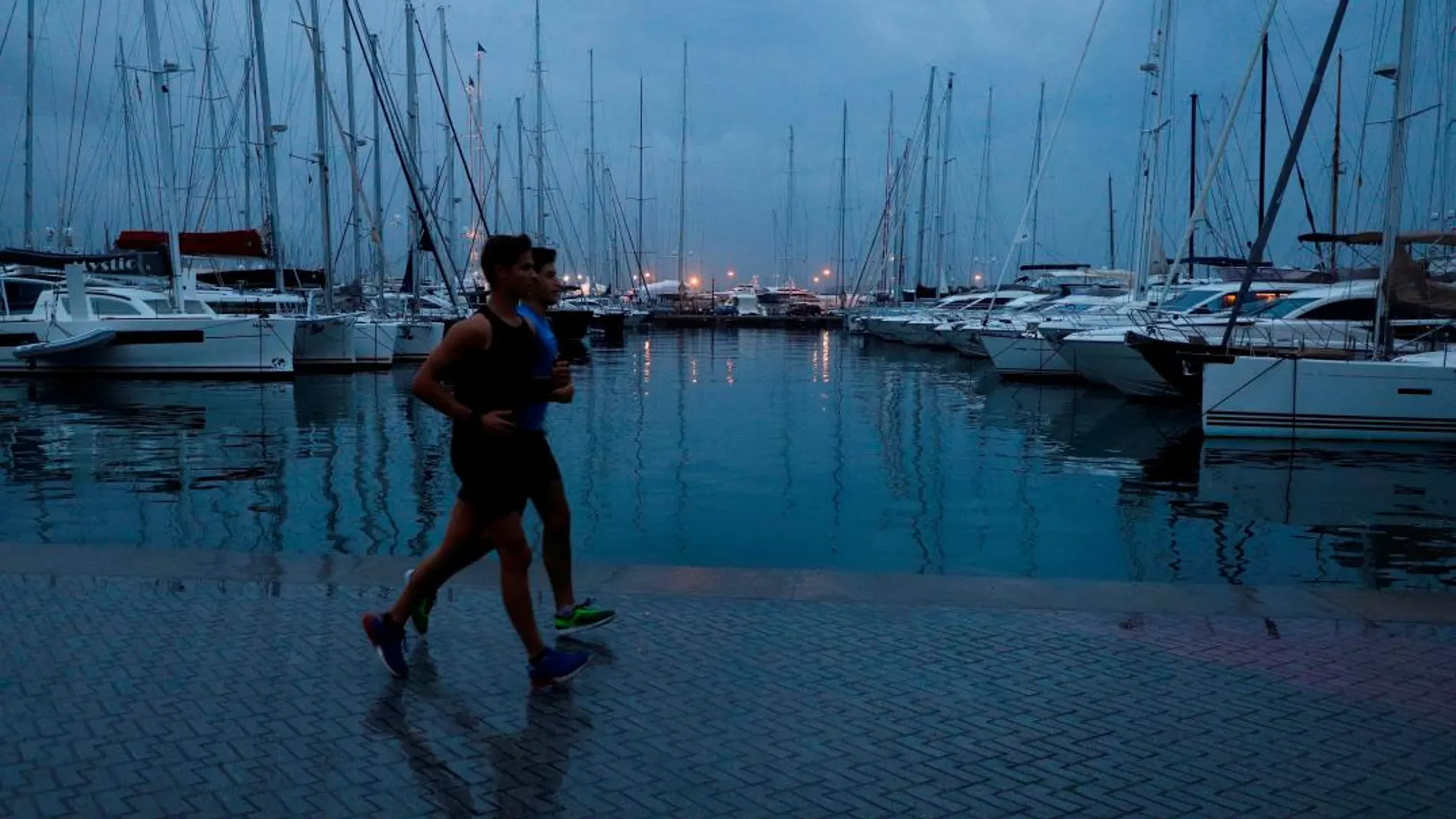 Dos personas corren por el paseo marítimo de Palma de Mallorca en un día con alerta por fuertes lluvias y tormenta en Baleares