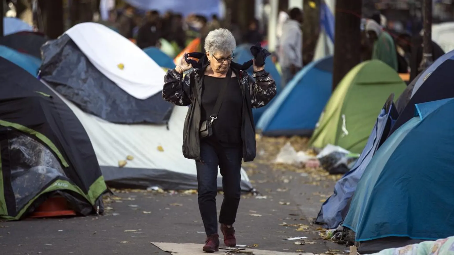 Una parisina pasea entre las tiendas de campaña de un campamento de migrantes en el distrito 19 de París