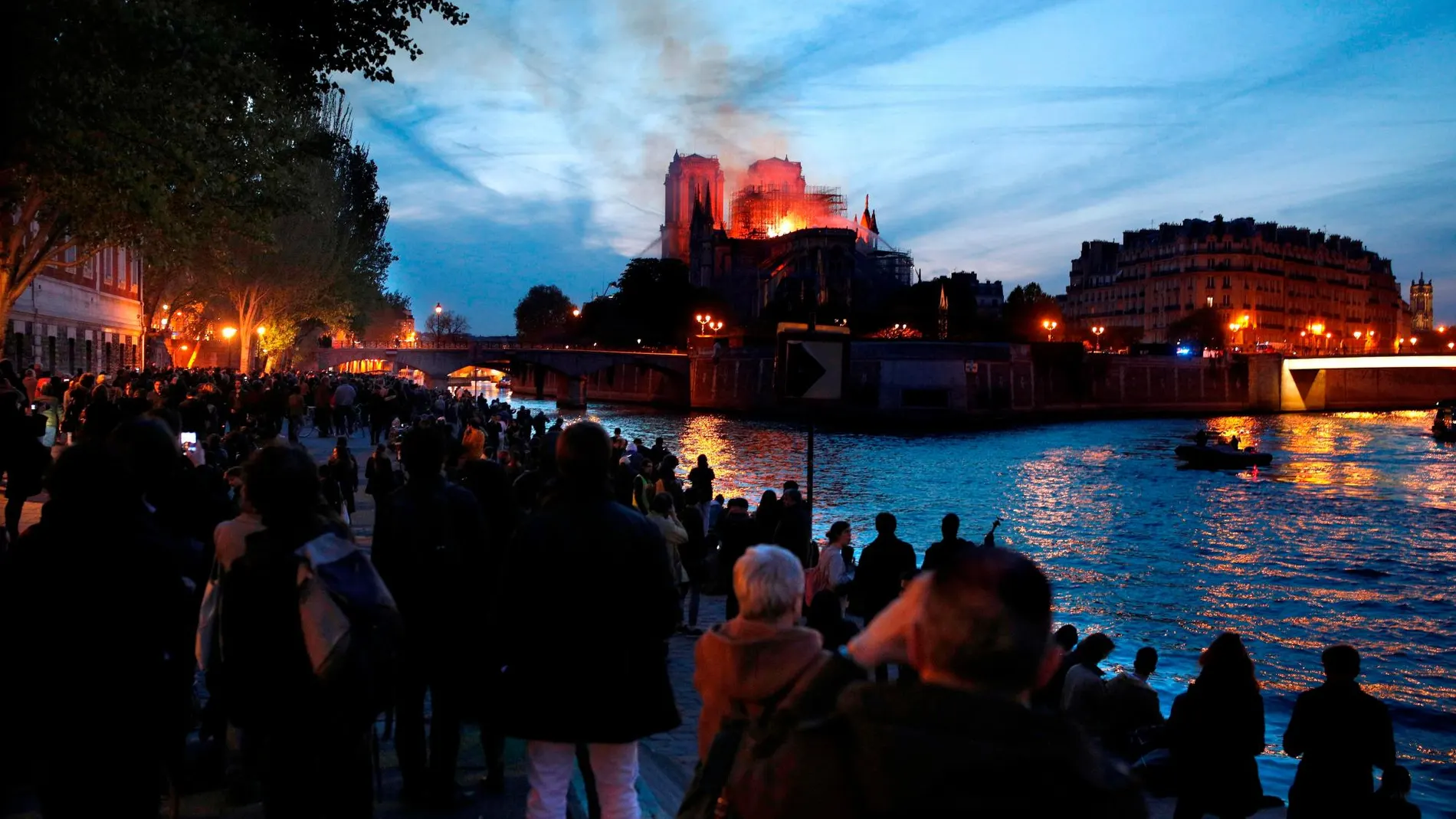 Decenas de personas en la orilla del Sena observan la columna de humo y las llamas que consumen a la catedral de Notre Dame. Efe