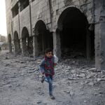 Un niño corre en Douma cerca de un edificio derruido