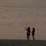 Dos jóvenes con su móvil en la playa / AP