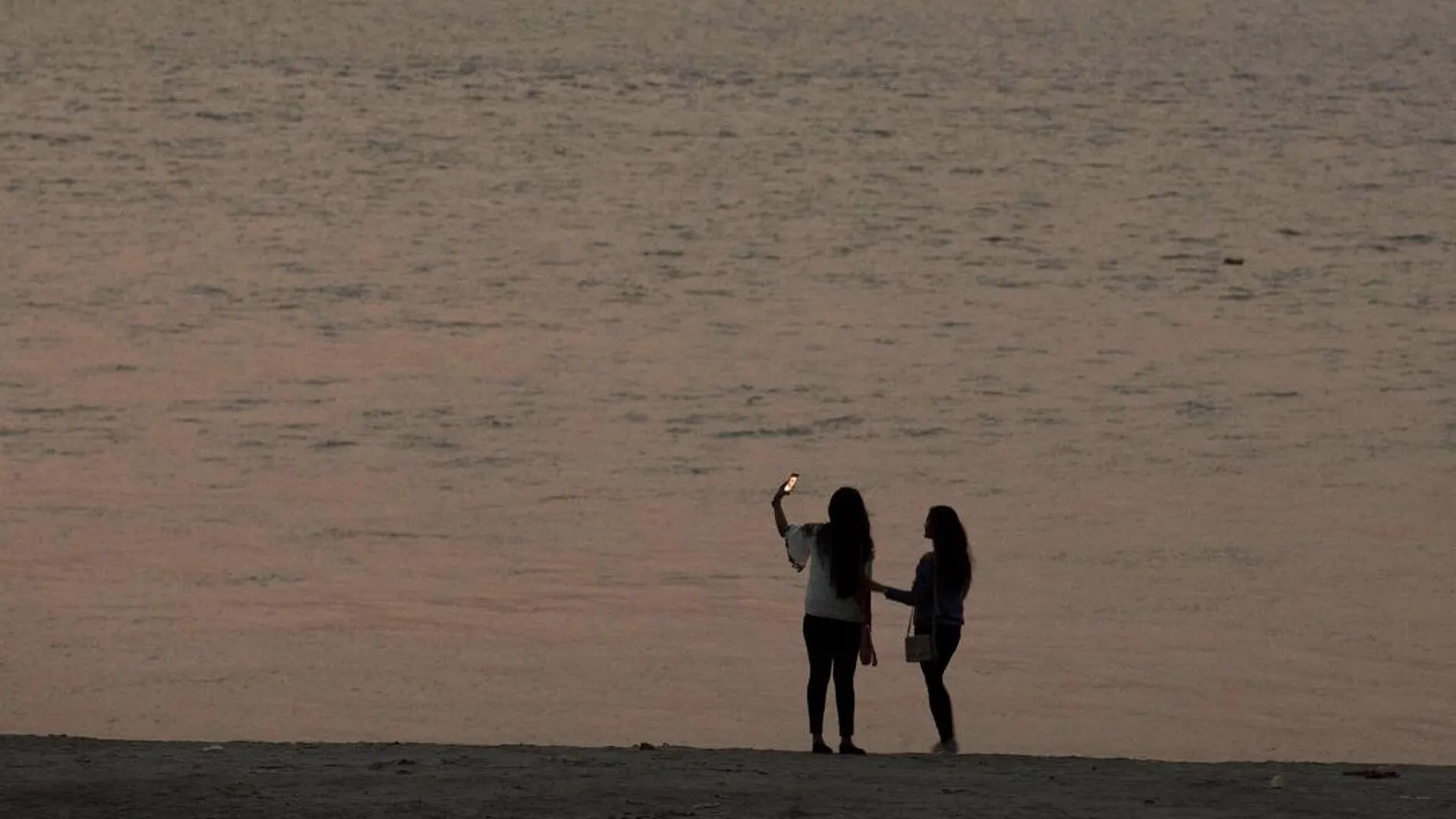 Dos jóvenes con su móvil en la playa / AP