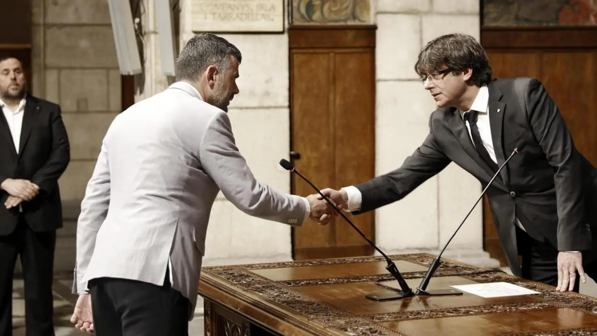 El presidente de la Generalitat, Carles Puigdemont, saluda al nuevo conseller de Empresa y Conocimiento, Santi Vila (i), tras su toma de posesión esta mañana en el Palau de la Generalitat