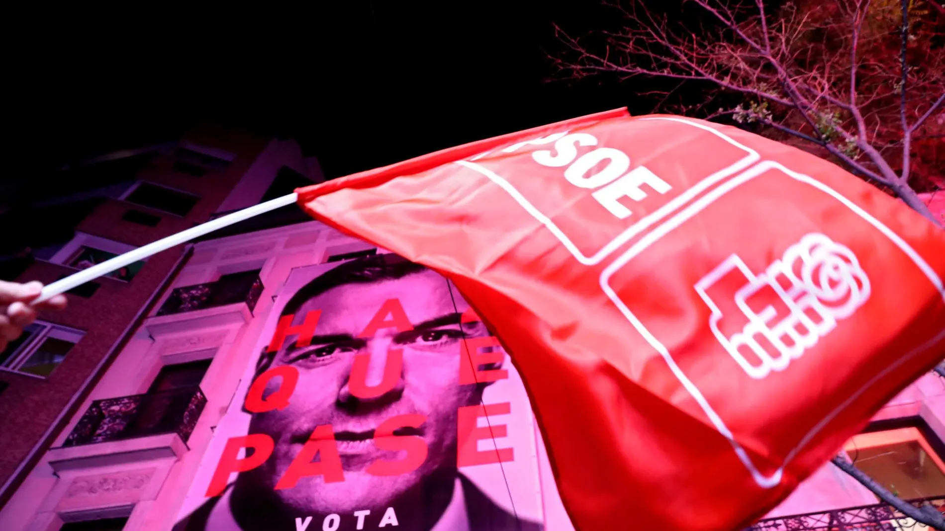 Una bandera del PSOE es ondeada con el cartel de la campaña electoral de Pedro Sánchez