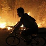 Un joven monta en bicicleta pegado a las llamas, ayer, en Galicia