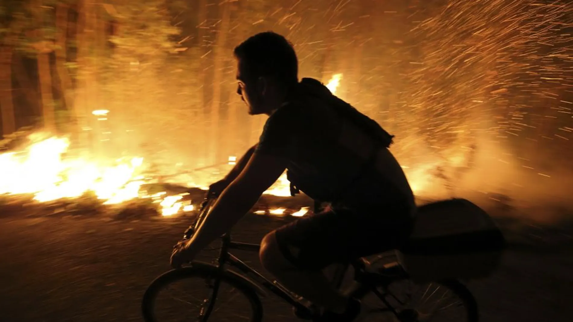 Un joven monta en bicicleta pegado a las llamas, ayer, en Galicia