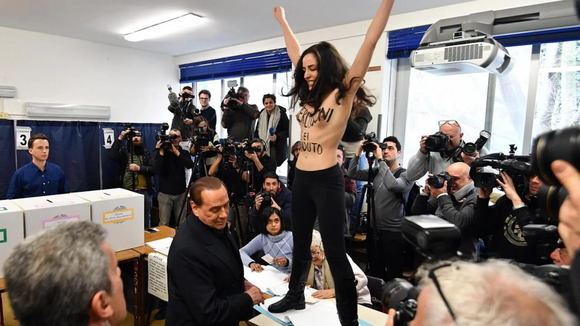 Una activista de Femem se planta sin camiseta delante de Berlusconi cuando se disponía a votar. Efe