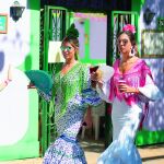 Dos jóvenes vestidas de flamenca pasean por una calle del Real de la Feria de Málaga.