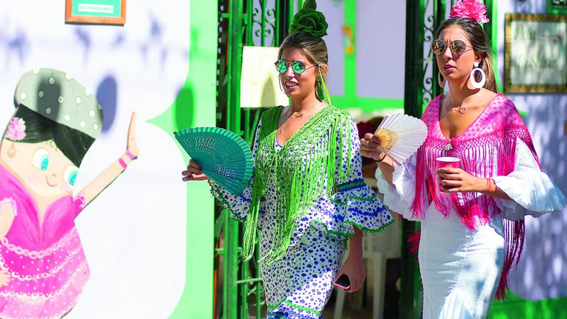 Dos jóvenes vestidas de flamenca pasean por una calle del Real de la Feria de Málaga.