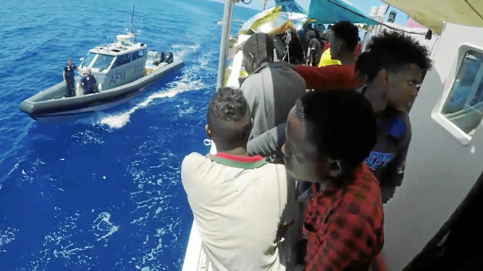 os inmigrantes que viajan a bordo del barco «Lifeline» observan la llegada de un buque maltés que les trae víveres tras cinco días a la deriva