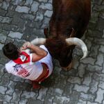 Un toro de la ganadería sevillana de Miura arrastra a un mozo a su paso en el tramo de entrada al callejón de la Plaza/ Efe
