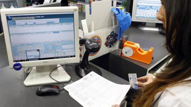 Farmacéutica comprueba la receta electrónica de un cliente en una oficina de farmacia de León
