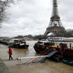 Un hombre camina sobre unos tablones prácticamente hundidos mientras el agua desborda el río Sena mientras la Torre Eiffel