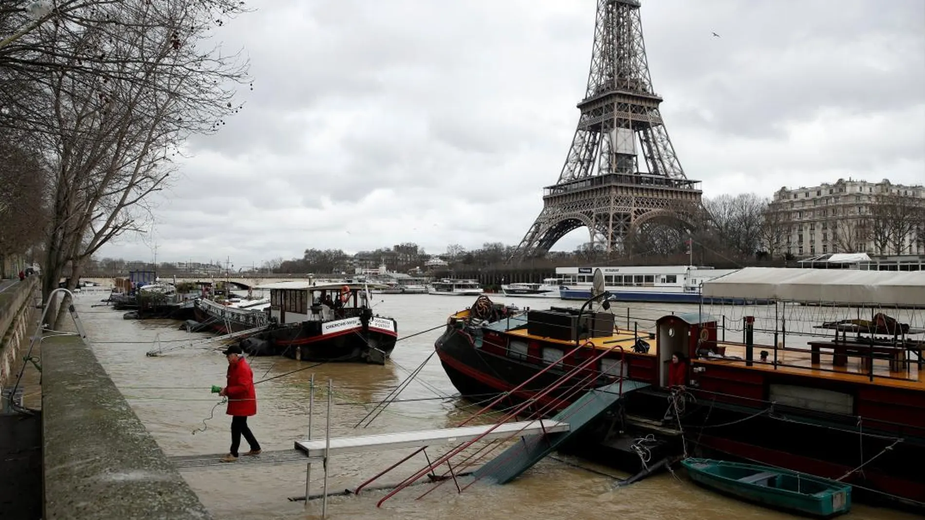 Un hombre camina sobre unos tablones prácticamente hundidos mientras el agua desborda el río Sena mientras la Torre Eiffel