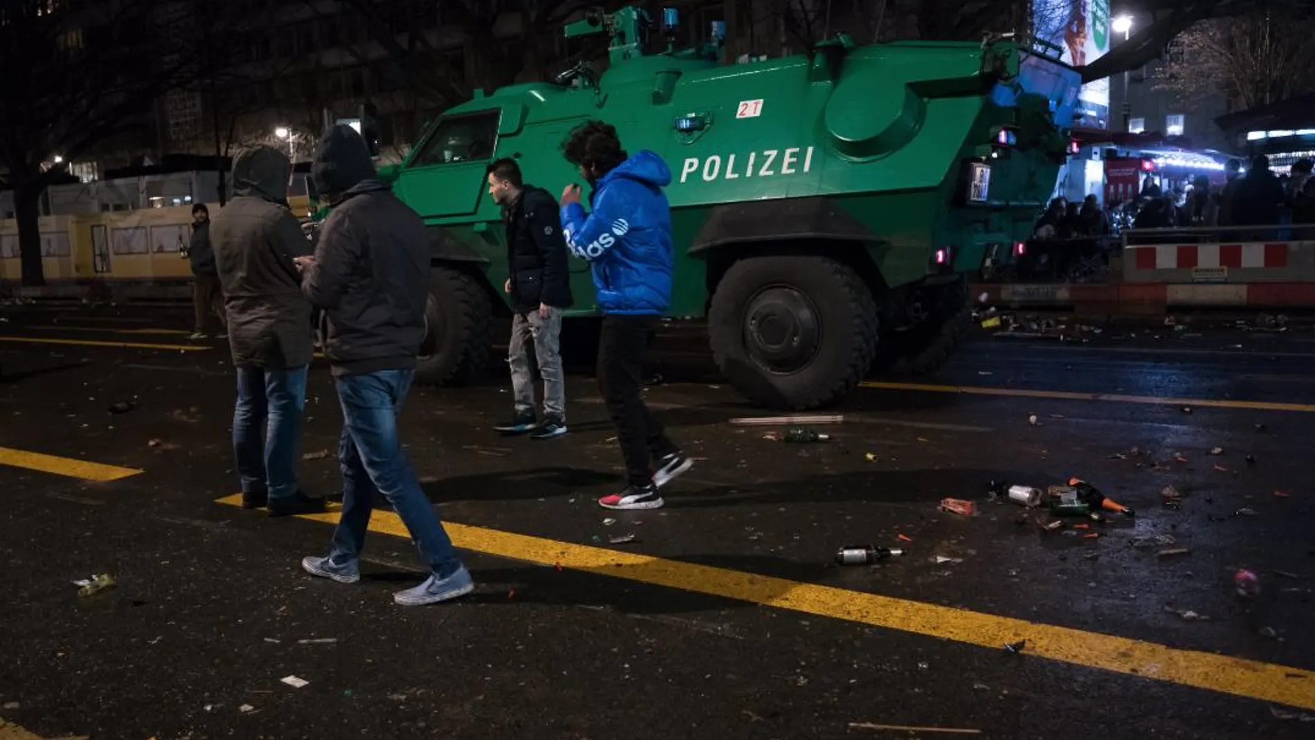 Varios jóvenes pasean junto a la Puerta de Brandenburgo, vigilada por un furgón policial blindado