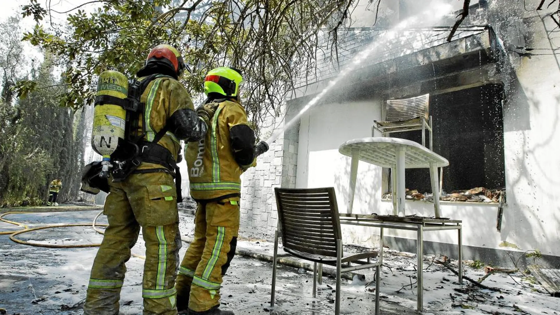 Dos bomberos tratan de sofocar las llamas en una vivienda de Marxuquera, en Gandía