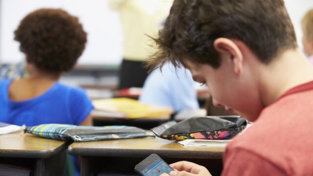 Un niño jugando con su teléfono móvil en clase / Dreamstime