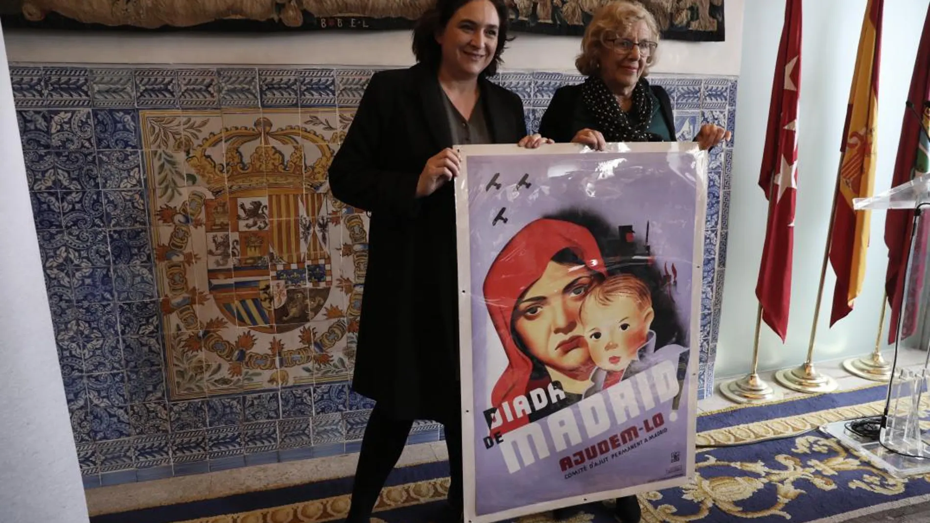 La alcaldesa de Madrid, Manuela Carmena (i), y de Barcelona, Ada Colau, posan junto al cartel regalo de Colau a la alcaldesa madrileña