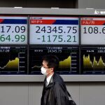 Un hombre camina junto a pantalla que muestra información bursátil en Tokio (Japón) hoy