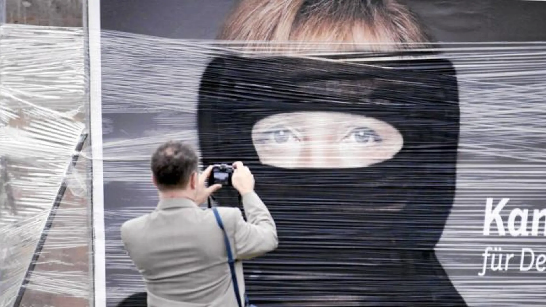 Un hombre hace una foto en Berlín a un cartel de Merkel saboteado con pintura negra