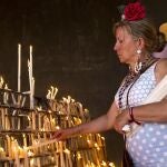 Una mujer vestida de flamenca coloca velas de ofrenda en el santuario de El Rocío, en Almonte (Huelva).