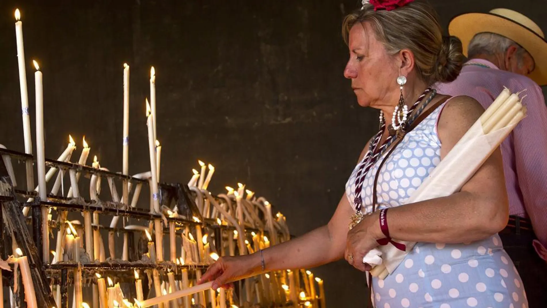 Una mujer vestida de flamenca coloca velas de ofrenda en el santuario de El Rocío, en Almonte (Huelva).