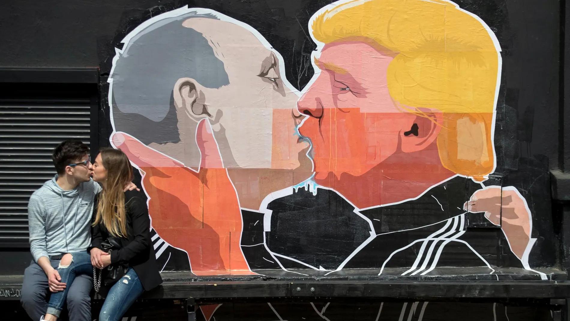 Imagen de archivo de unos jóvenes besándose enfrente de un grafiti de Putin y Trump