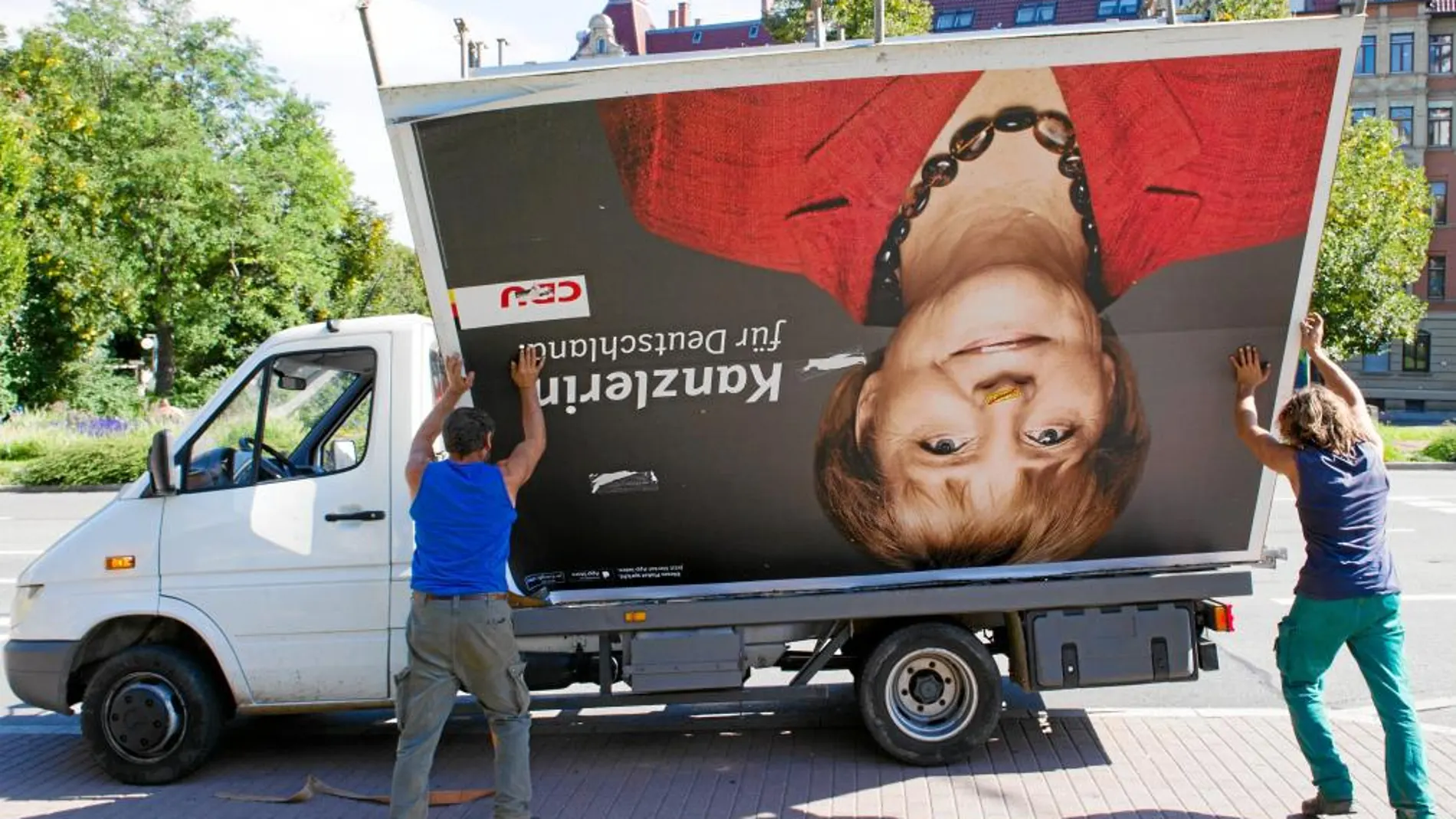 Varios trabajadores desmontan un cartel electoral de Angela Merkel en Stuttgart