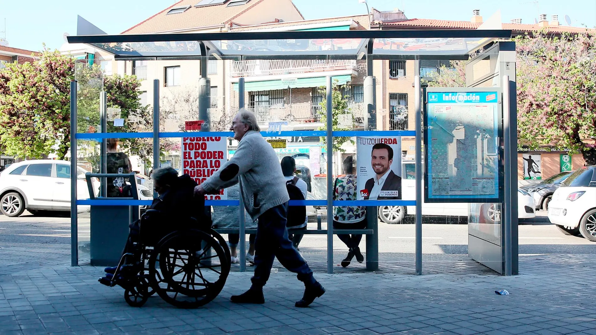 Una persona ayuda a mover a otra que va en silla de ruedas