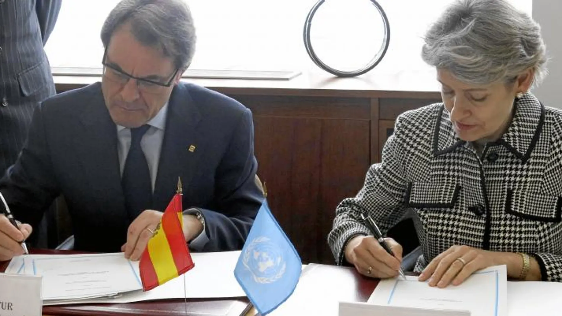 Mas, con la directora general de la Unesco en la firma del protocolo, ayer en París, con la bandera española sobre la mesa