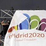 Unos operarios recogen una pancarta de Madrid 2020 en la Puerta de Alcalá