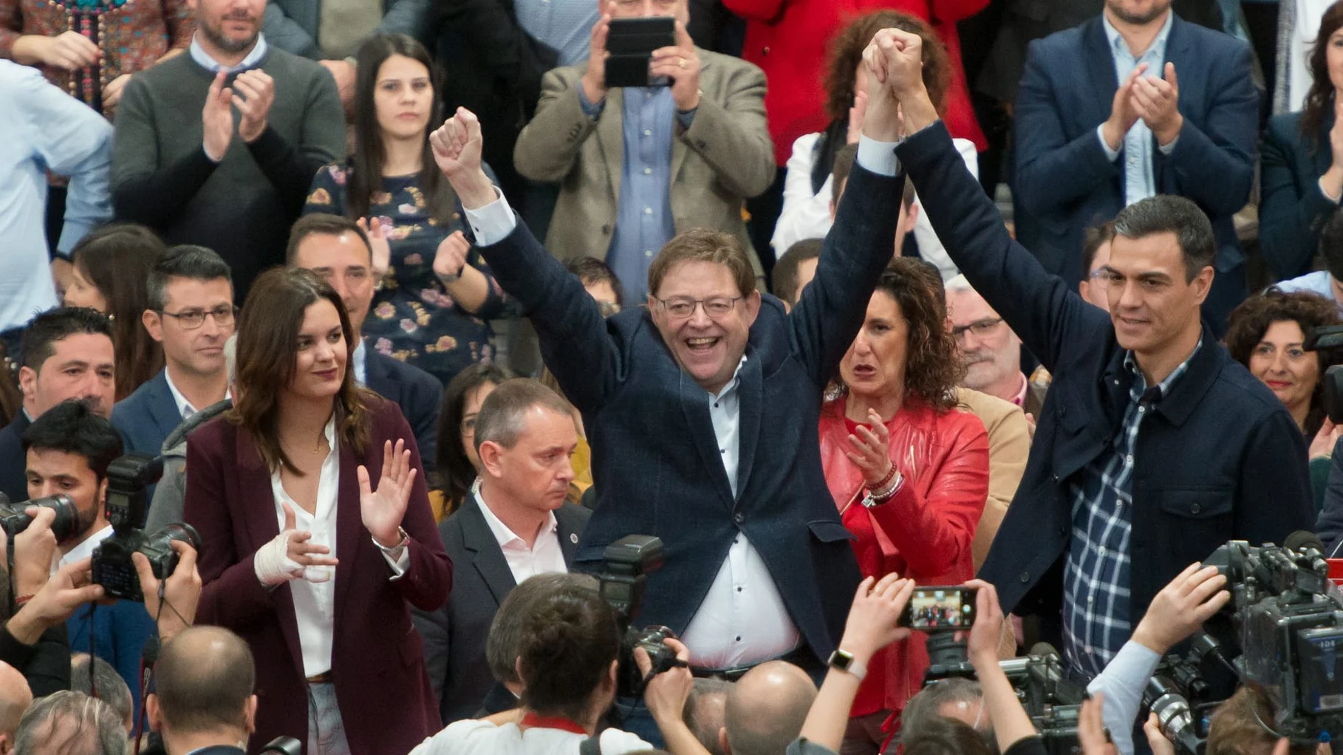 Pedro Sánchez levanta el brazo a Ximo Puig, mientras Sandra Gómez, a la izquierda, aplaude en el acto de su presentación como candidata a la alcaldía de Valencia, celebrado ayer en el Polideportivo de El Cabanyal