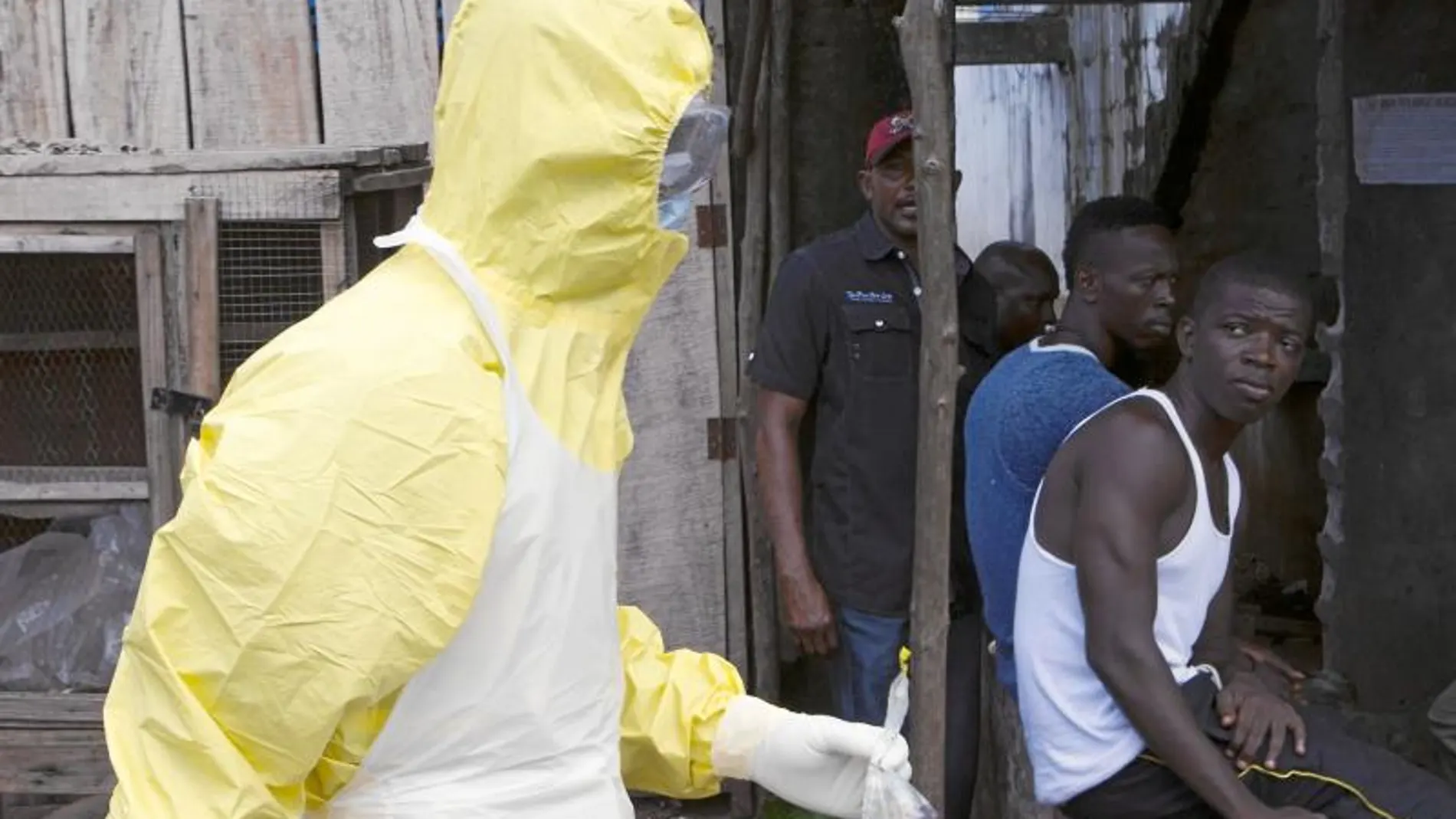 Varios jóvenes de Sierra Leona observan a un sanitario equipado con el mono que marca el protocolo para atender a enfermos de ébola