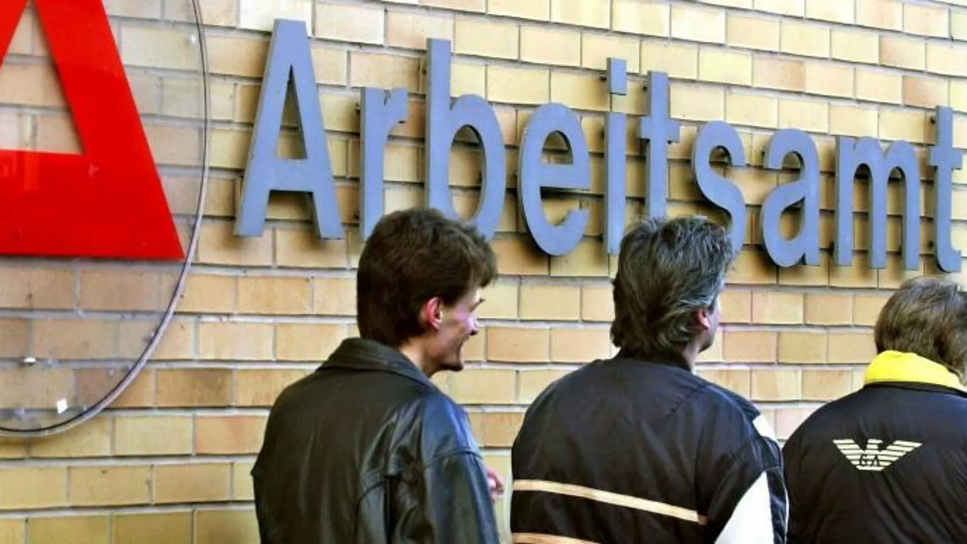 Tres hombres delante de la entrada de una oficina estatal de desempleo en Saarbruecken, Alemania.