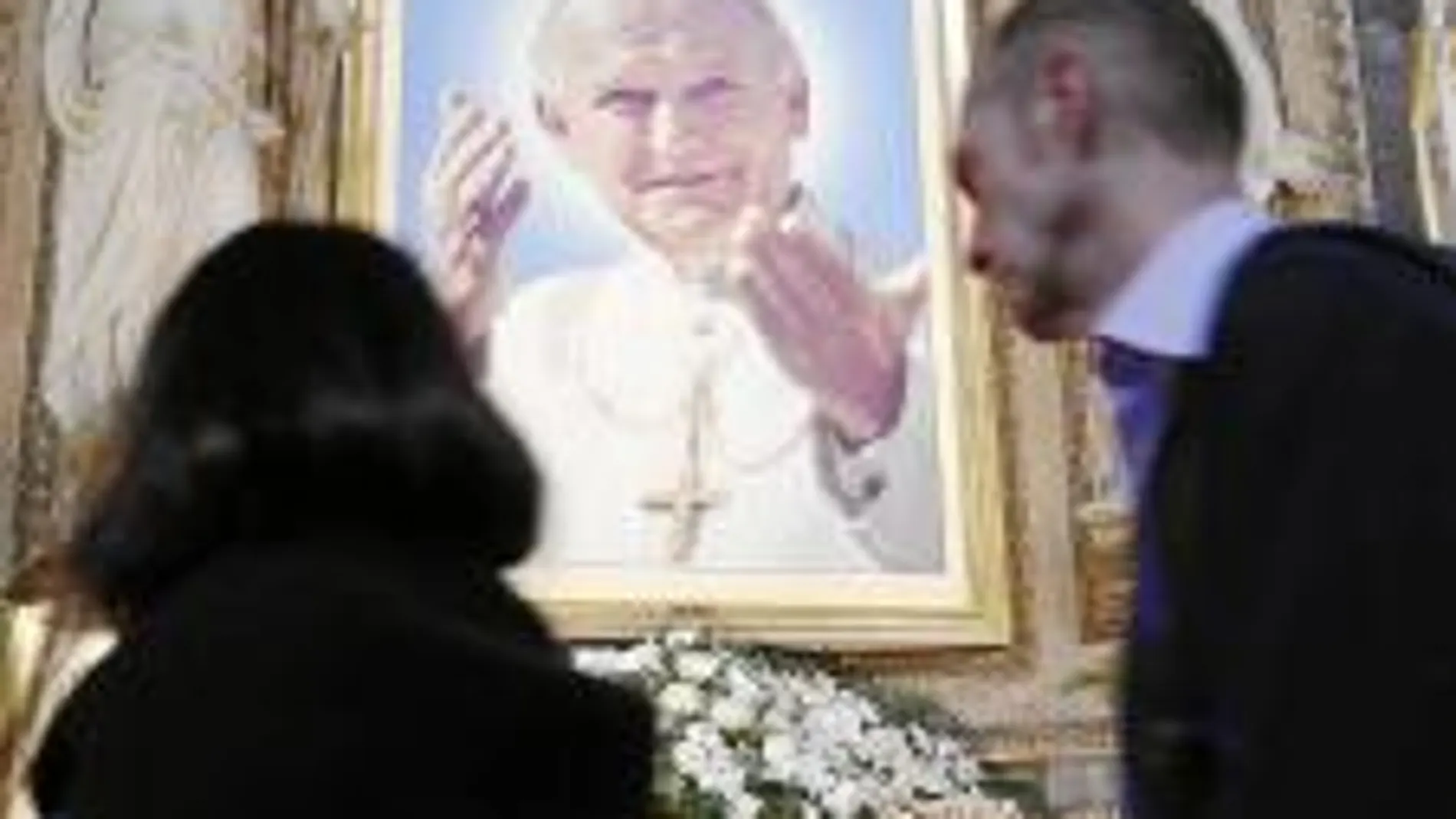 Varios fieles pasan frente a una imagen del Pontífice Juan Pablo II, situada en el altar de una iglesia en el centro de la ciudad de Roma.