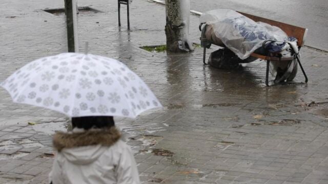 Un hombre duerme en un banco bajo la lluvia