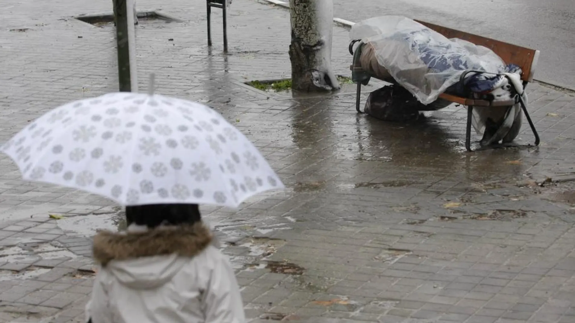 Un hombre duerme en un banco bajo la lluvia